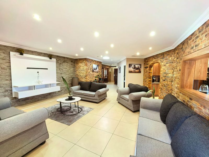 Spacious living room featuring exposed brick walls, built-in media cabinetry, recessed lighting, and neutral ceramic floor tiles.