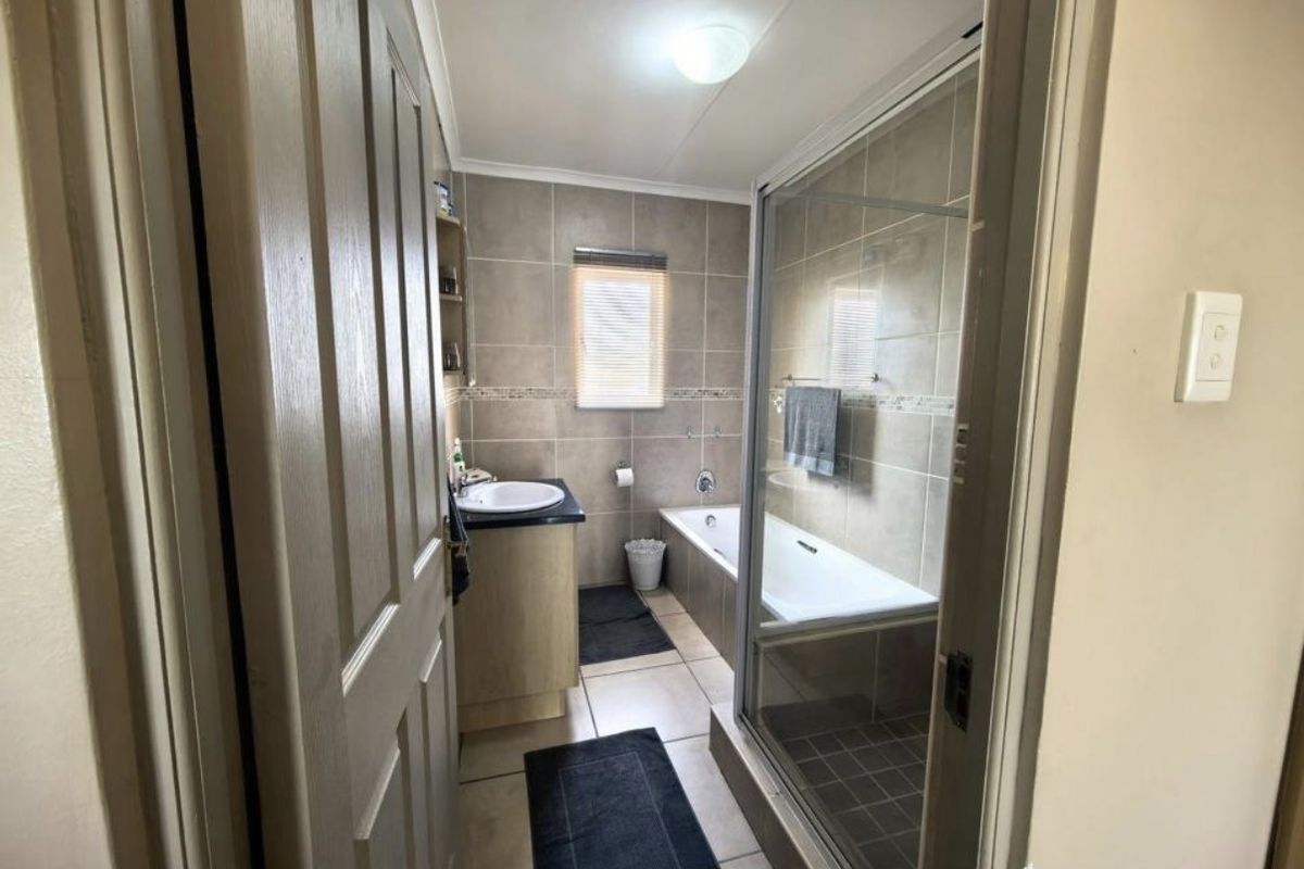 A functional bathroom featuring a built-in vanity, a bathtub, and a separate glass-enclosed shower with neutral wall and floor tiling.