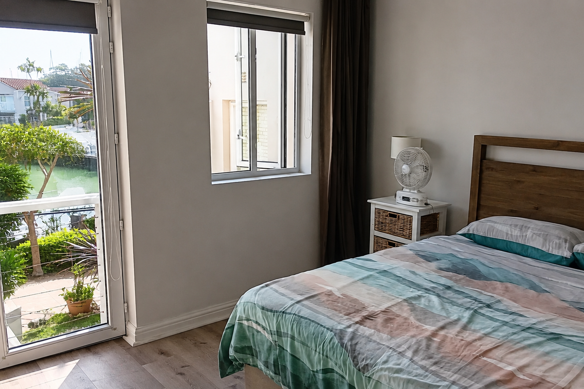A bright bedroom featuring laminate flooring, a glass door leading to a balcony, and a window with views of the surrounding area.