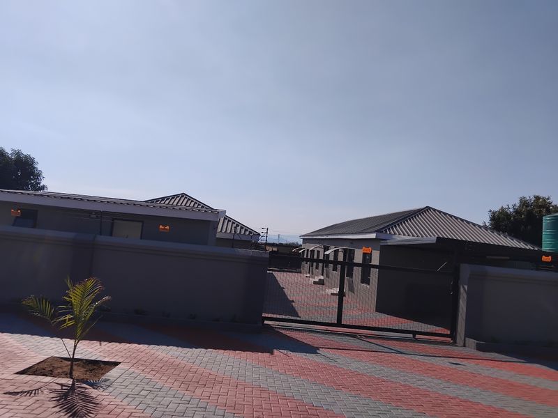 A modern apartment complex exterior featuring a paved driveway, secure perimeter wall, and metal sliding gate entrance.