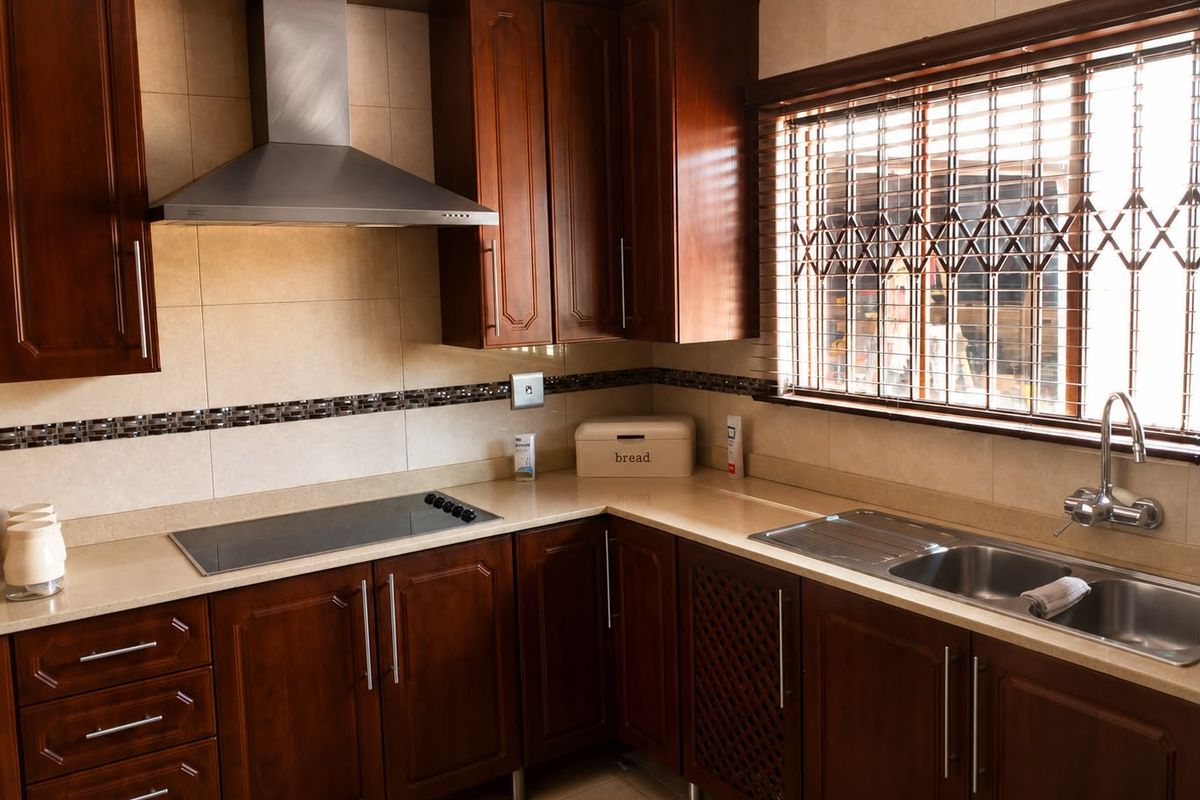 A functional kitchen featuring dark wood cabinetry, stone countertops, a stainless steel extractor fan, an induction hob, and a double-basin sink.