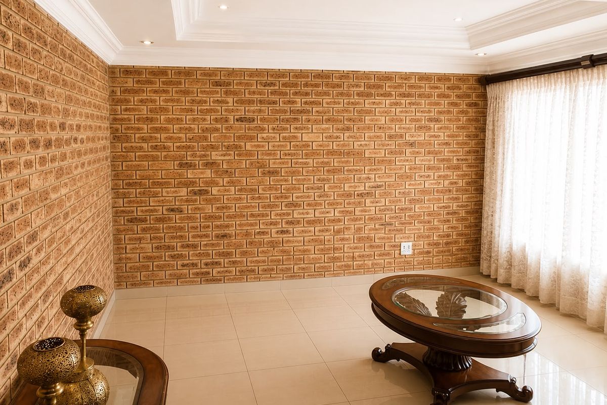 A spacious living room featuring exposed face-brick feature walls, recessed ceiling detailing with downlights, and polished floor tiles.