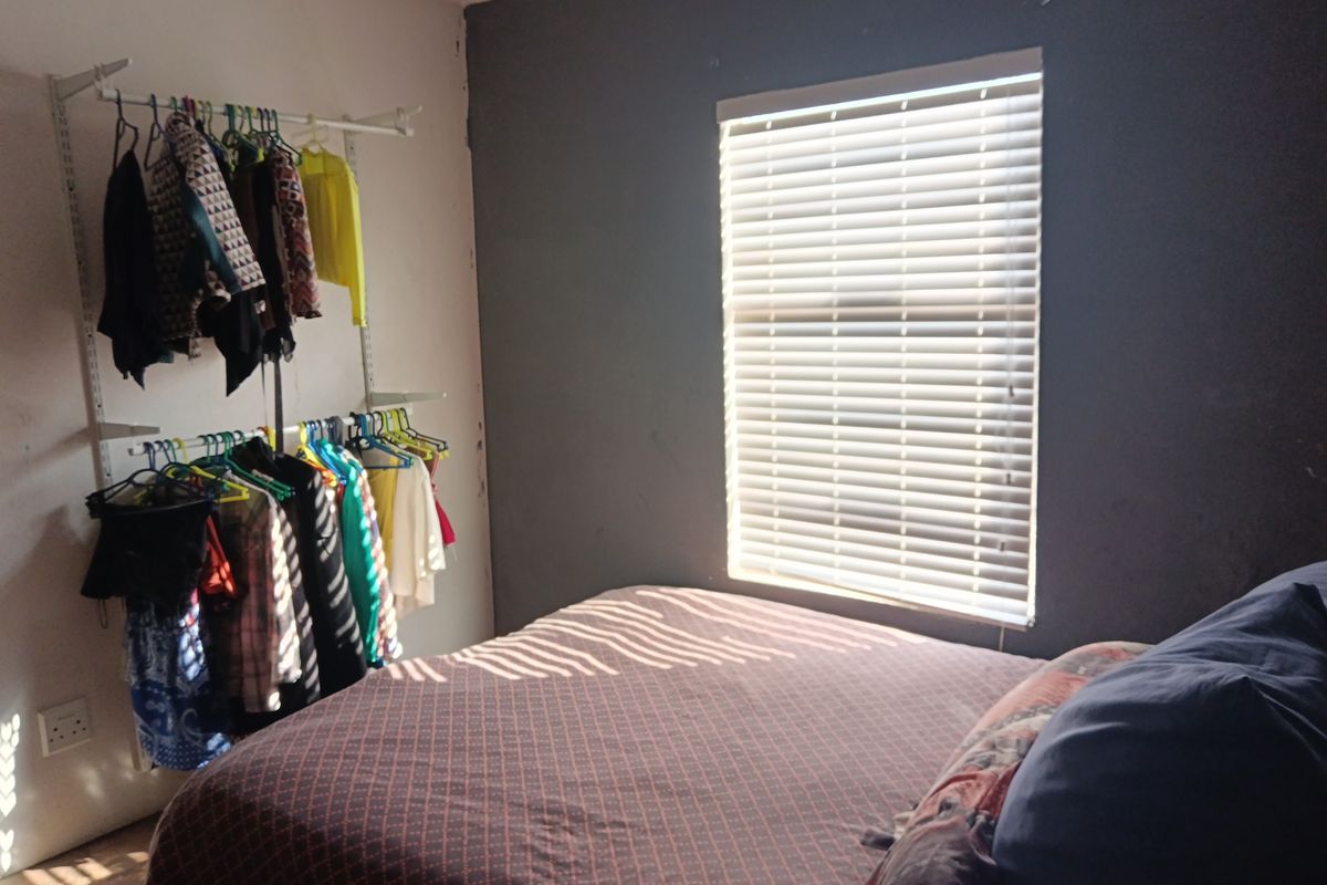 A bedroom featuring a dark accent wall, fitted window blinds, and an open-style wall-mounted clothing rail system.