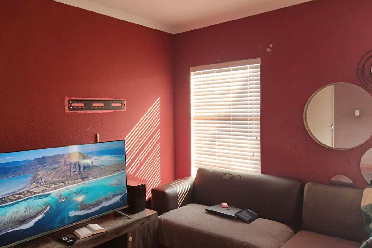 A living room featuring red textured walls, a window with fitted blinds, and a wall-mounted television bracket.