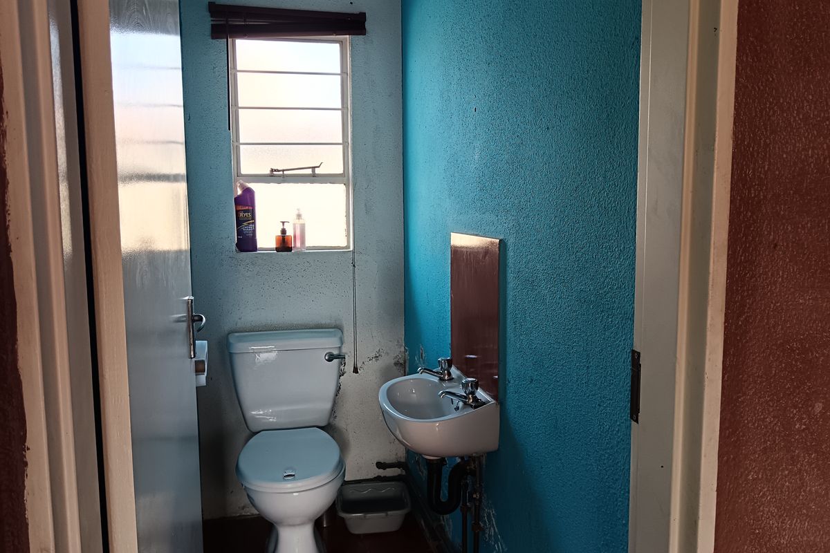 A small, dated bathroom featuring a toilet and wall-mounted basin with visible wall surface wear and exposed plumbing.
