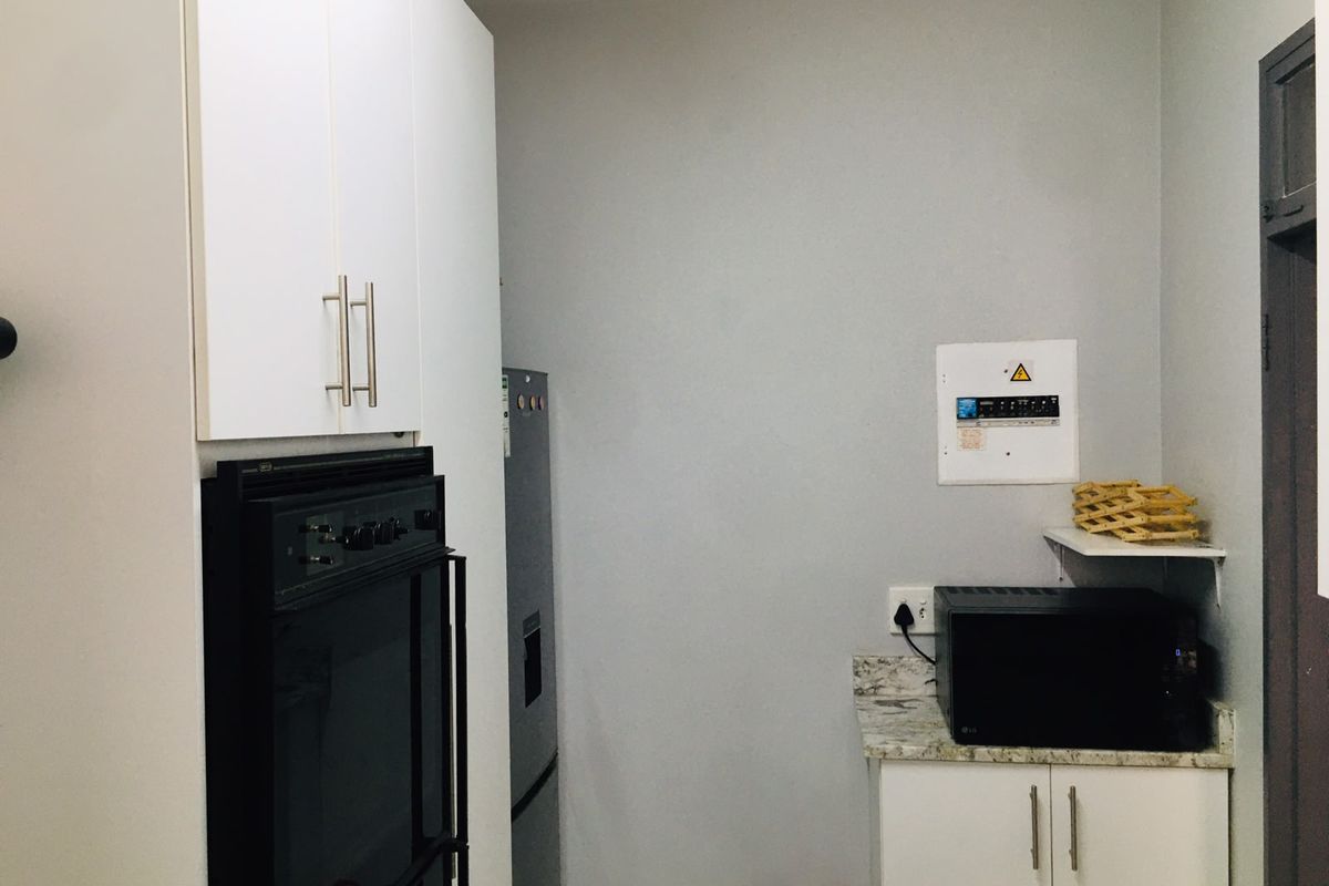 A functional kitchen area featuring built-in cabinetry, a wall-mounted oven, and stone-look countertops with integrated electrical distribution board.