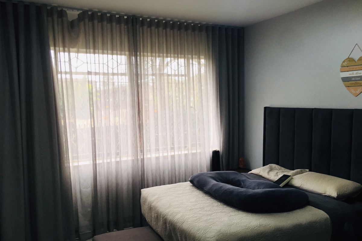 A well-lit bedroom featuring large windows with floor-to-ceiling curtains and tiled flooring.