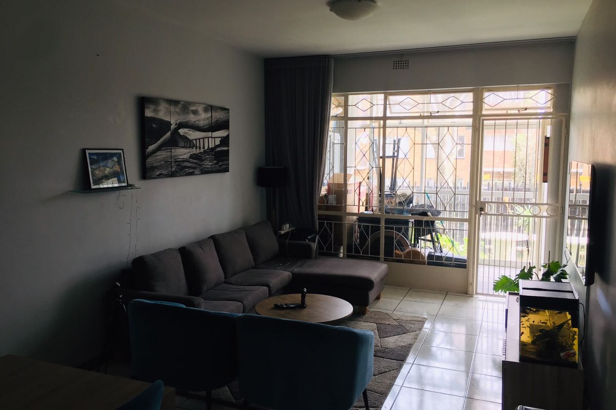 A living room featuring tiled flooring and a large glass sliding door with security gate leading to an outdoor area.