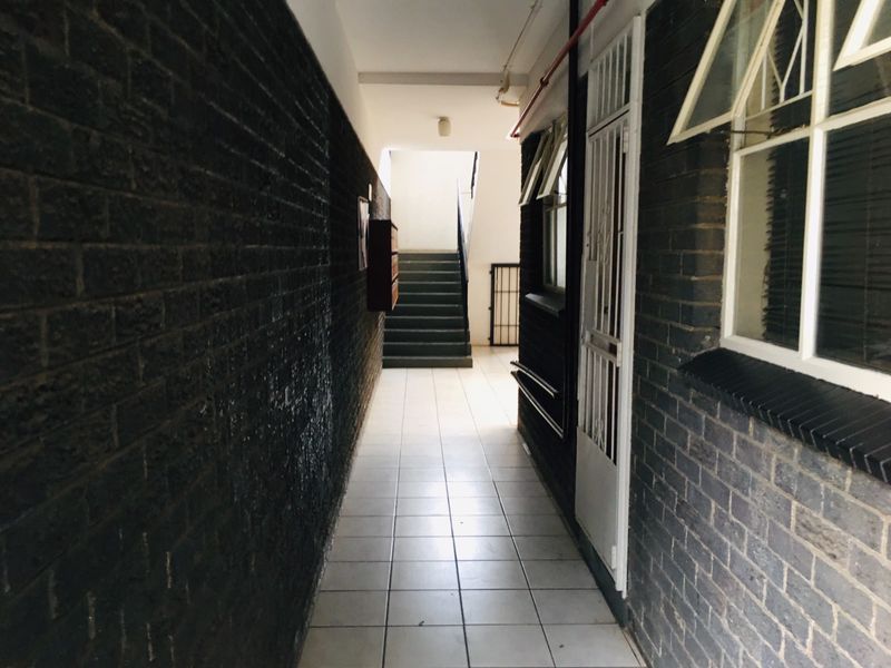 A communal hallway featuring dark brick walls, tiled flooring, and access to a staircase, providing a functional transition space within the apartment building.