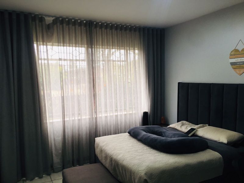 A well-lit bedroom featuring large windows with floor-to-ceiling curtains and tiled flooring.