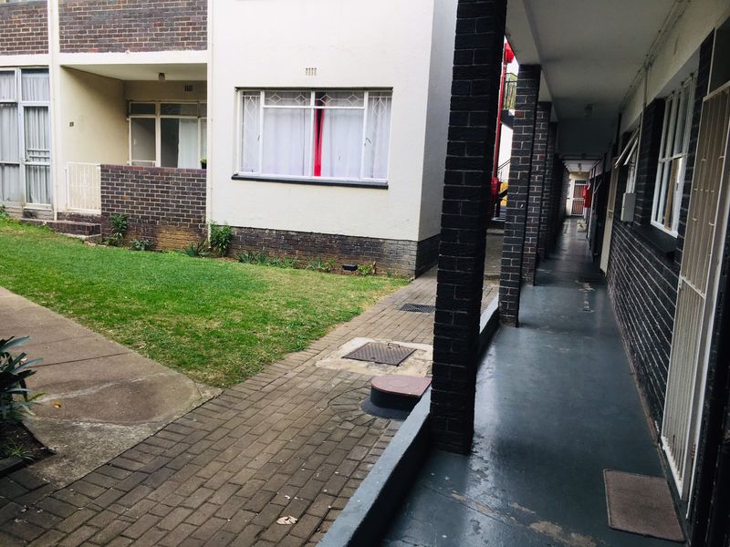A view of the exterior walkway and communal garden area of the flat complex, featuring brick pillars and paved pathways.