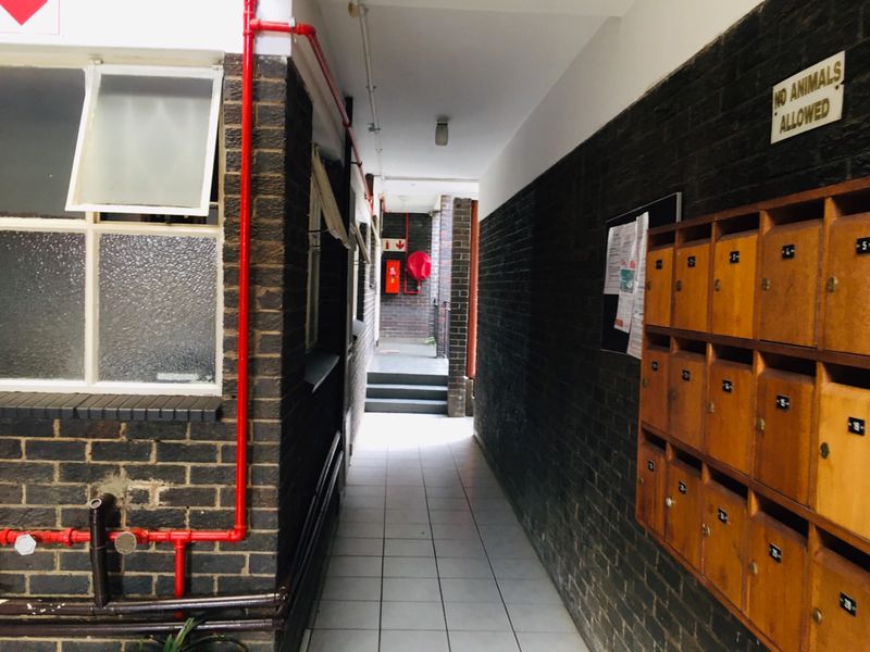 A communal hallway featuring tiled flooring, exposed red fire piping, and a bank of wooden mailboxes mounted on a dark brick wall.