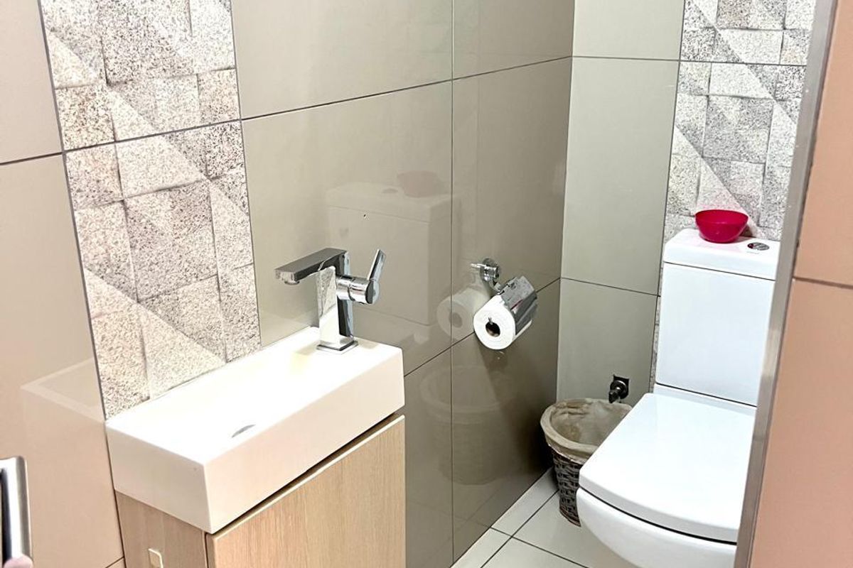 A modern guest bathroom featuring a compact vanity with a sleek basin, chrome faucet, and a contemporary toilet with tiled wall accents.