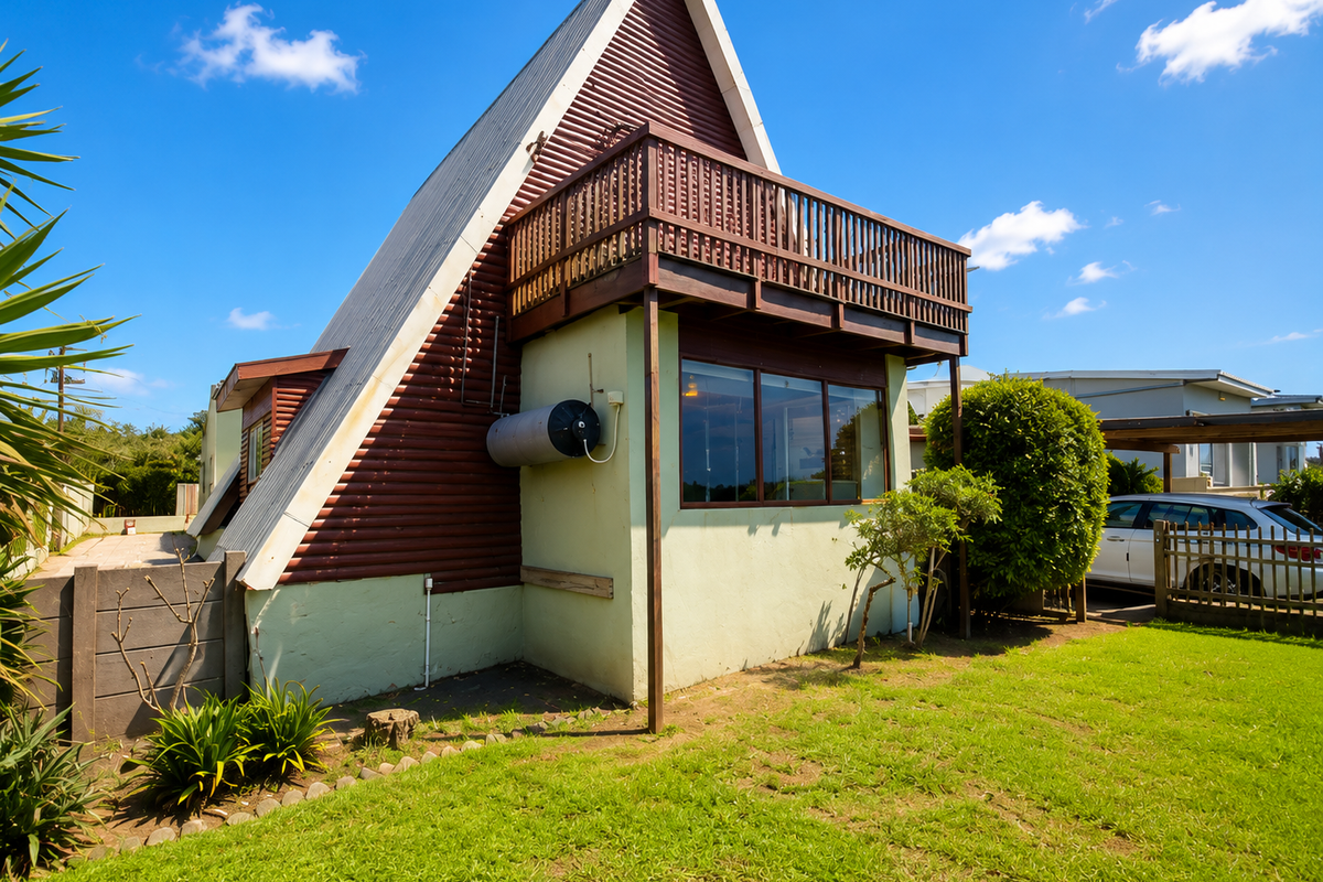 A-frame house exterior featuring a prominent upper-level wooden balcony, corrugated metal roof, and a private garden area with established landscaping.