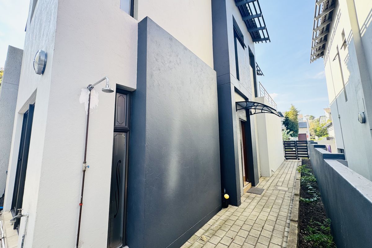 Side exterior walkway of the townhouse featuring paved path, modern dark grey accent wall, and an outdoor shower fixture.
