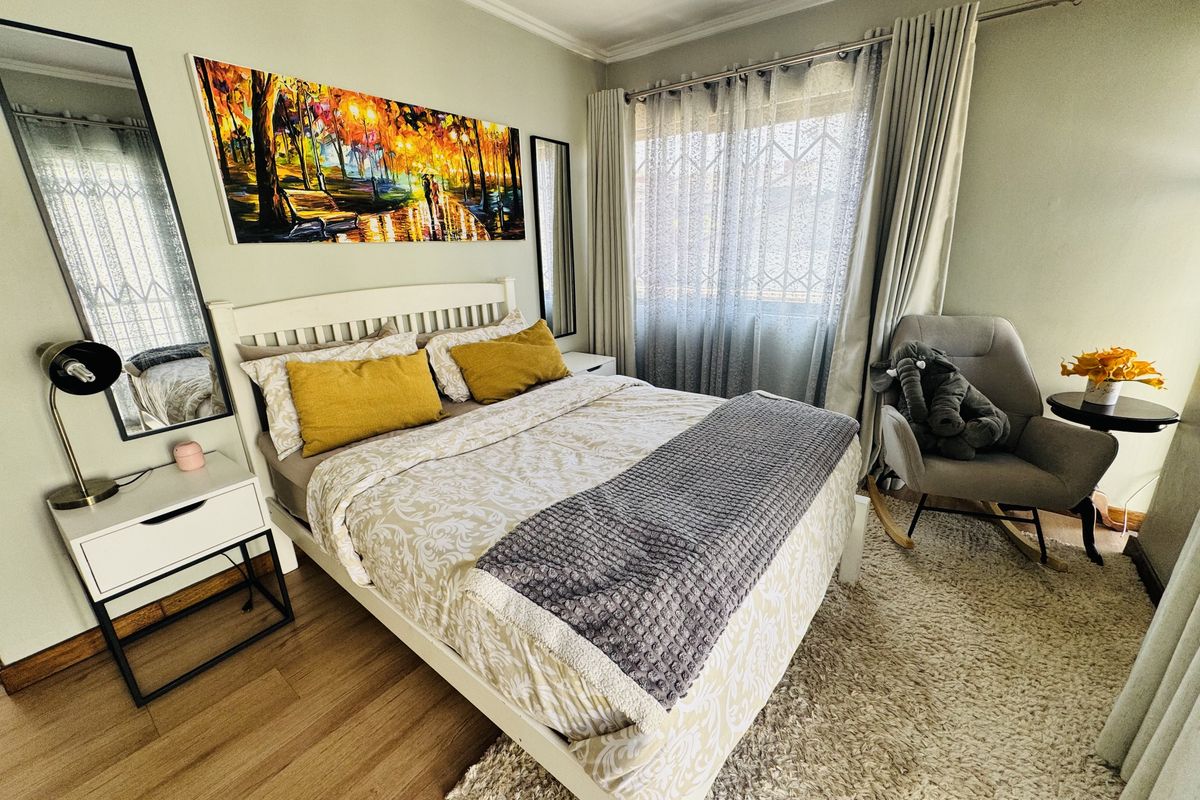A well-maintained bedroom featuring light wood-look flooring, crown molding, and a window fitted with security bars and curtains.