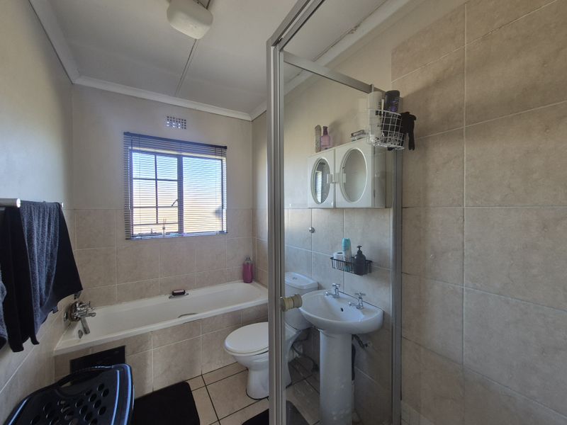 A functional bathroom featuring a bathtub, pedestal basin, toilet, and a separate shower enclosure with neutral wall and floor tiling.