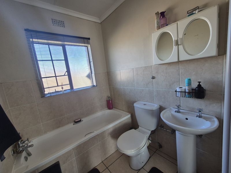 A functional bathroom featuring a bathtub, pedestal basin, toilet, and wall-mounted medicine cabinet with neutral wall and floor tiling.