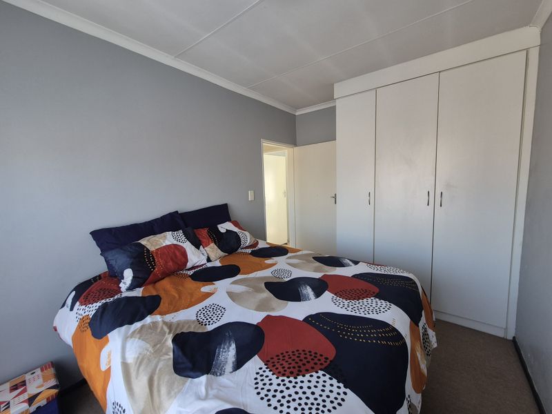 A functional bedroom featuring a built-in wardrobe with white cabinetry and neutral wall finishes.