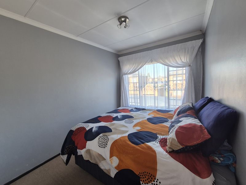 A functional bedroom featuring carpeted flooring, a coved ceiling, and a window fitted with security bars.