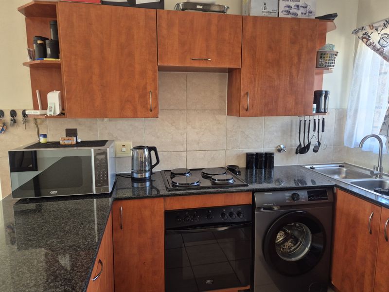 A functional kitchen featuring wood-finish cabinetry, granite countertops, a tiled backsplash, built-in oven, electric hob, and an integrated washing machine.