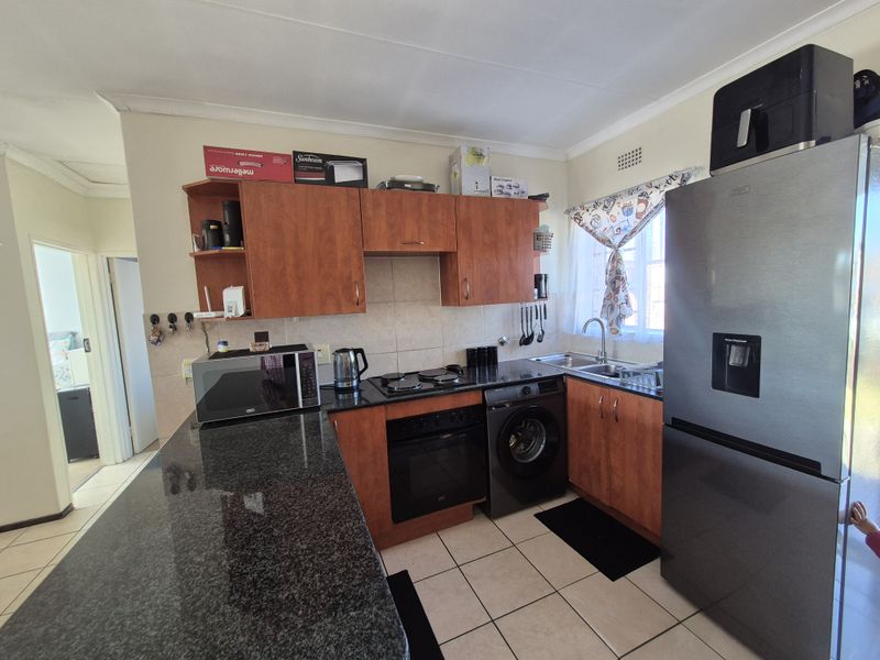 Functional kitchen featuring granite countertops, laminate cabinetry, built-in oven, electric hob, and tiled flooring with an integrated laundry appliance space.