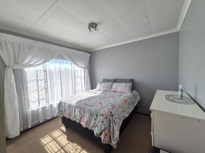 A well-lit bedroom featuring neutral grey walls, carpeted flooring, and large windows with installed curtain rails.