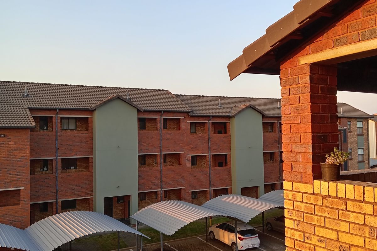 View of the apartment complex exterior featuring brick facade, tiled roofing, and covered parking bays for residents.