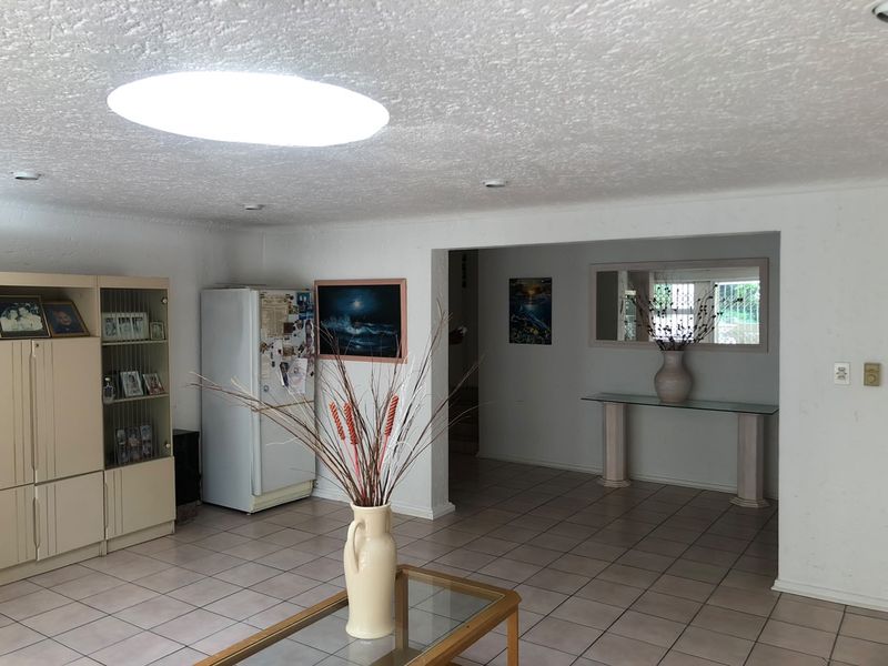 Spacious open plan living area featuring neutral floor tiles, a large circular skylight, and a seamless transition into the adjacent hallway.