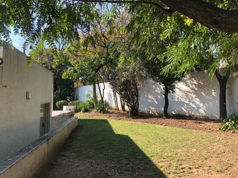 A private rear garden area featuring a lawn, mature trees, and high boundary walls, offering a secluded outdoor space for the property.