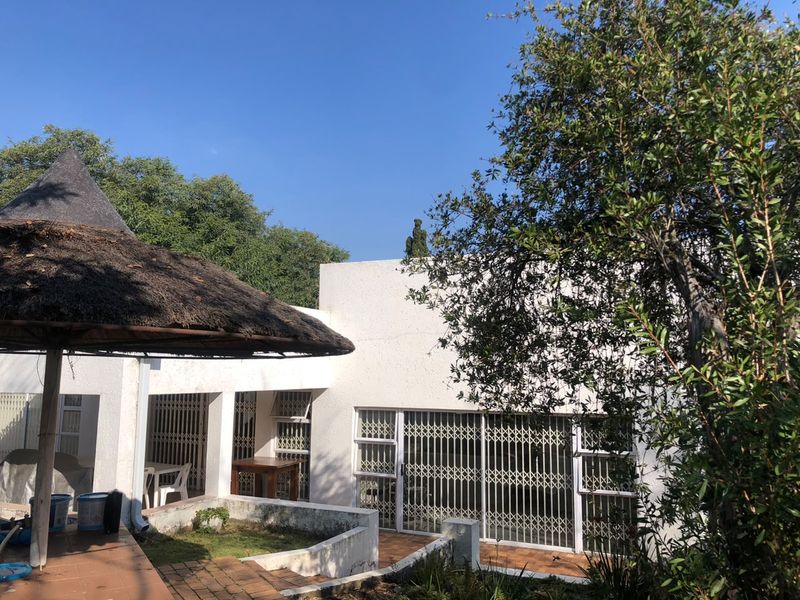 Rear exterior view featuring a covered patio area with a thatched roof, tiled flooring, and security gates leading into the home.