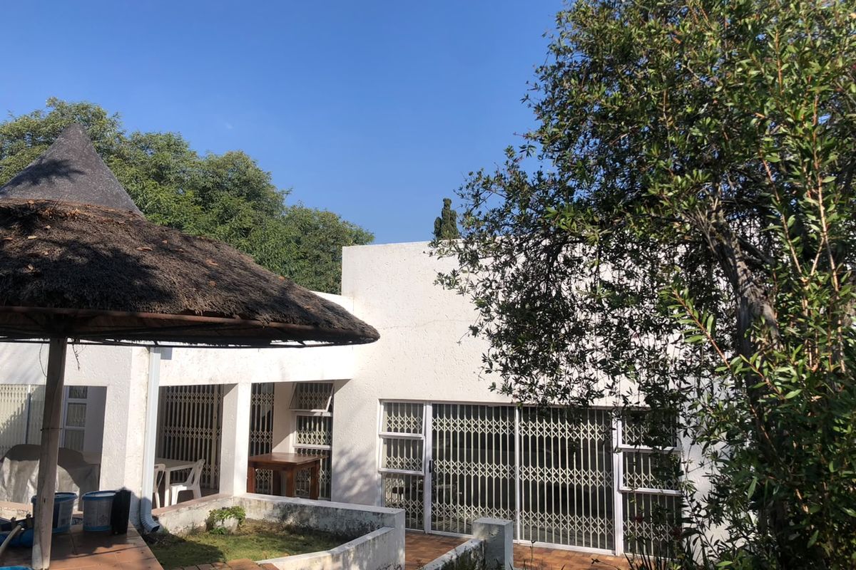Rear exterior view featuring a covered patio area with a thatched roof, tiled flooring, and security gates leading into the home.