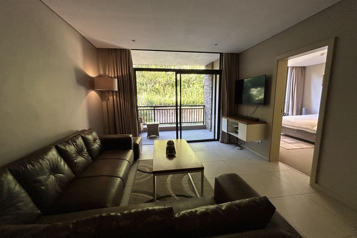 A well-maintained living room featuring large sliding glass doors leading to a private balcony, with tiled flooring and recessed lighting throughout.