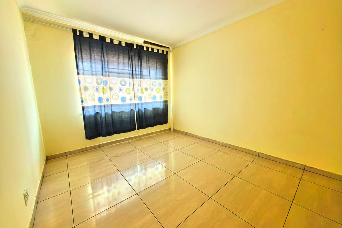 A bright, empty bedroom featuring neutral wall paint, tiled flooring, and a window with fitted curtain tracks.