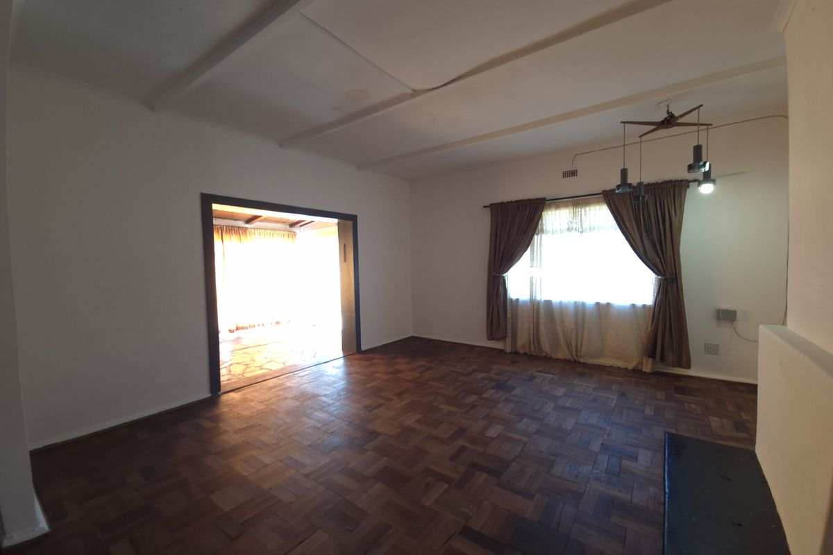 Spacious living room featuring original parquet flooring, large window with curtains, and a wide doorway leading to an adjacent room.