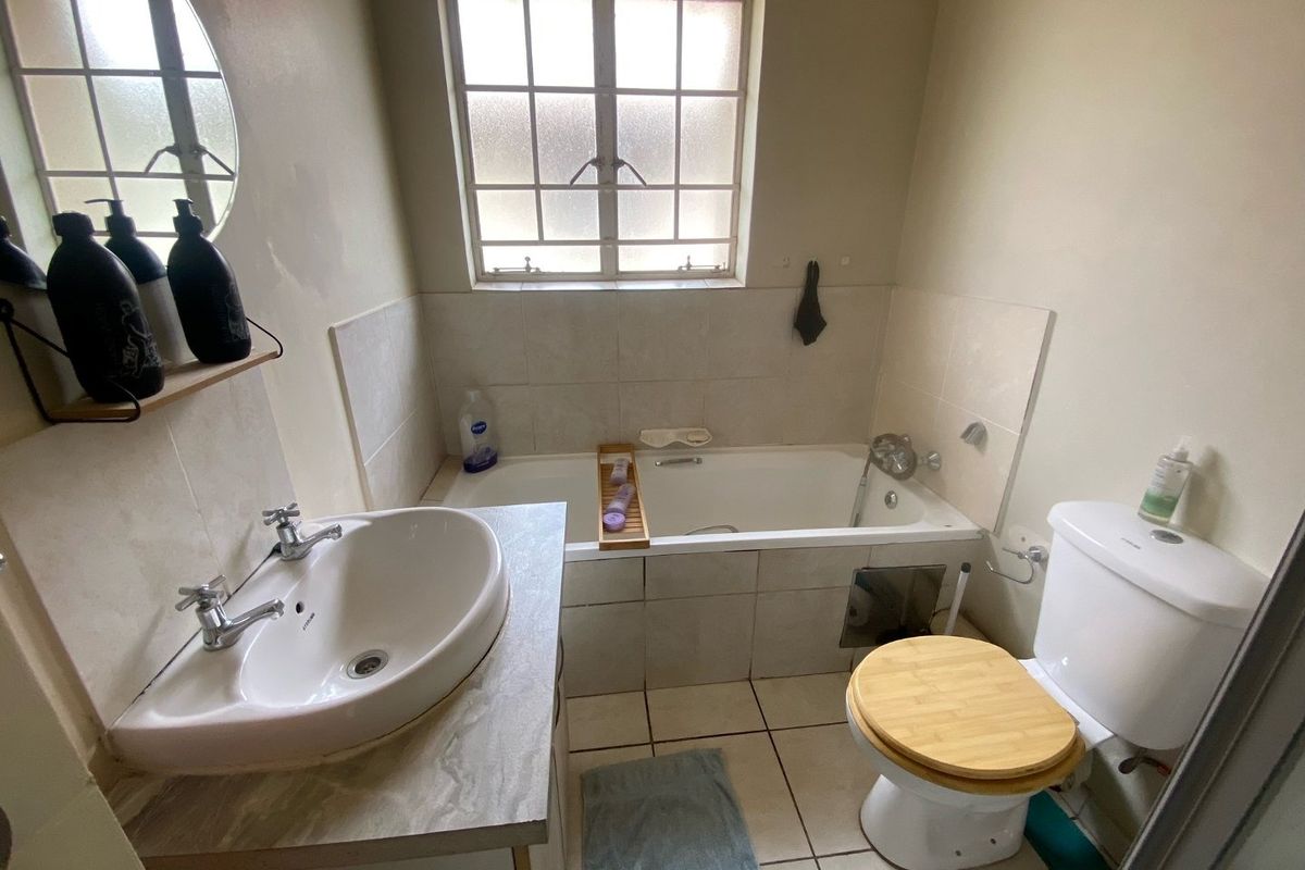 A functional bathroom featuring a built-in bathtub, a vanity basin with countertop, and a toilet, illuminated by a window with security bars.