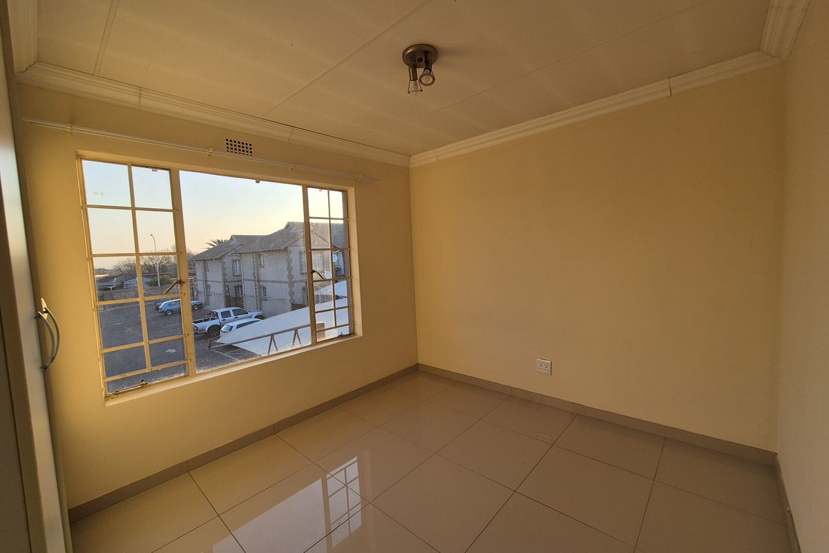 An empty bedroom featuring tiled flooring, a large window with security bars, and a simple ceiling light fixture.