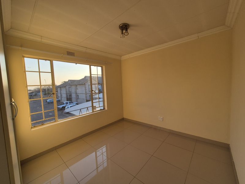 An empty bedroom featuring tiled flooring, a large window with security bars, and a simple ceiling light fixture.