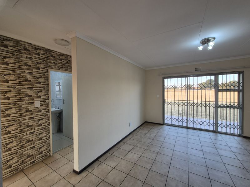 An open-plan living area featuring tiled flooring, a decorative stone-cladding feature wall, and sliding glass doors with security gates leading to the exterior.