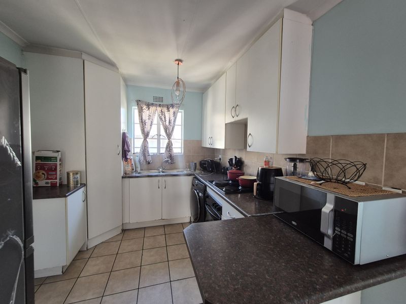 A functional kitchen featuring white cabinetry, dark laminate countertops, tiled backsplash, and ceramic floor tiles, offering a practical layout for daily meal preparation.