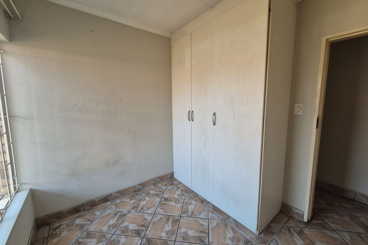 A bedroom featuring built-in cupboards, tiled flooring, and a large window, offering a functional and neutral space ready for personalization.