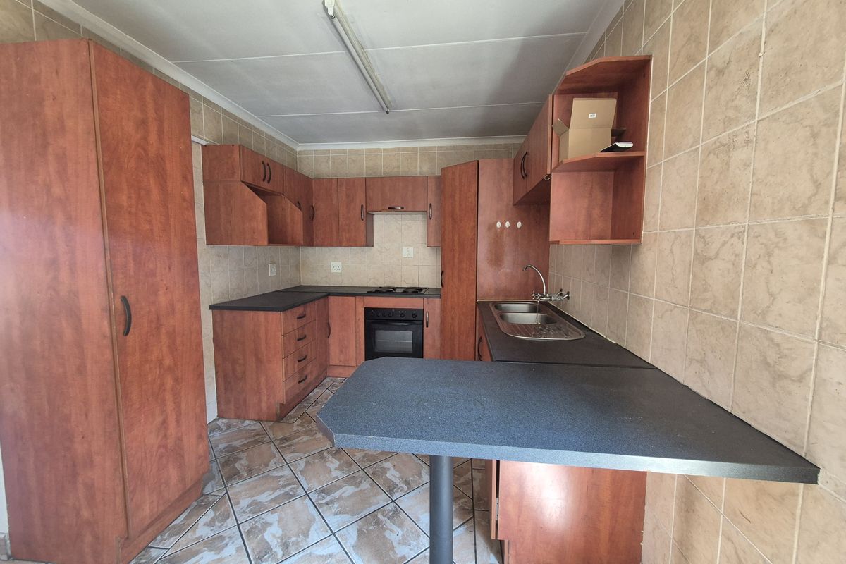 A functional kitchen featuring wood-look cabinetry, dark laminate countertops, a built-in oven and hob, and tiled flooring throughout.