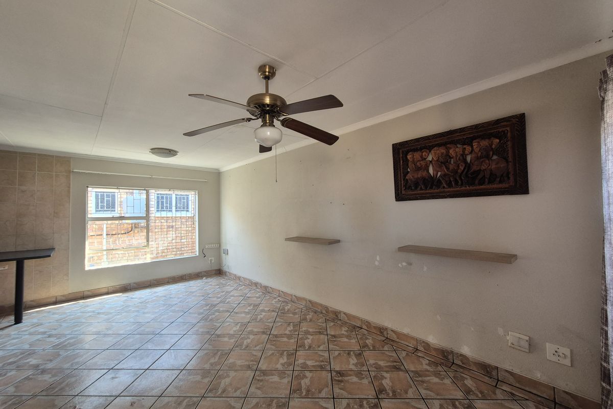 A spacious living area featuring tiled flooring, a ceiling fan, and large windows providing natural light.