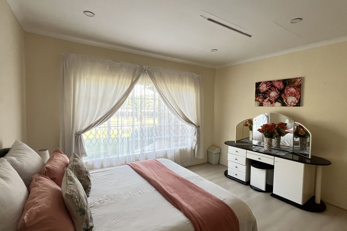 A well-lit bedroom featuring neutral walls, recessed ceiling lighting, and large windows with security bars, providing a comfortable and functional living space.