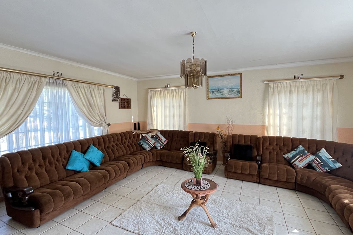Spacious living room featuring tiled flooring, large windows with curtain rails, and a central light fixture.