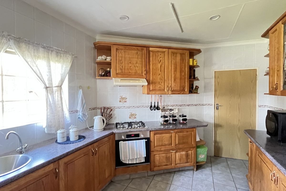 A functional kitchen featuring solid wood cabinetry, a built-in oven with gas hob, extractor fan, and tiled flooring with a neutral backsplash.