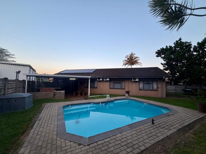 Rear exterior view featuring a swimming pool, paved surround, covered patio area with built-in braai, and solar panels installed on the roof.