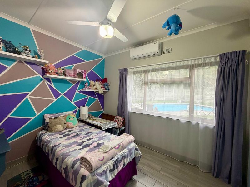 A bedroom featuring tiled flooring, a ceiling fan, a split-system air conditioner, and built-in wall shelving, with a view overlooking the pool area.
