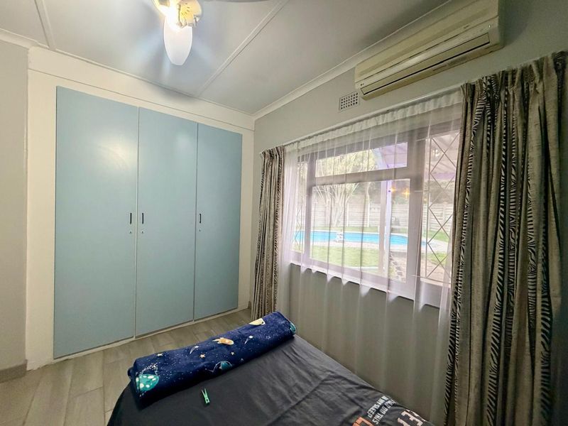 A bedroom featuring built-in cupboards, a split-system air conditioner, and a ceiling fan, with a view overlooking the backyard pool area.