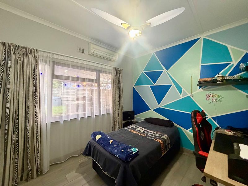 A bedroom featuring tiled flooring, a ceiling fan, and a wall-mounted split-system air conditioner, with a decorative geometric painted feature wall.